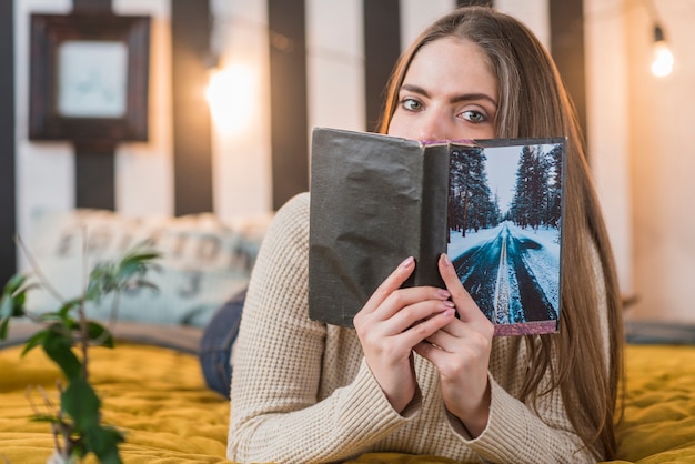 Woman lying on bed covering her mouth with book