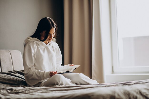 Женщина, лежа на кровати и читающая книгу