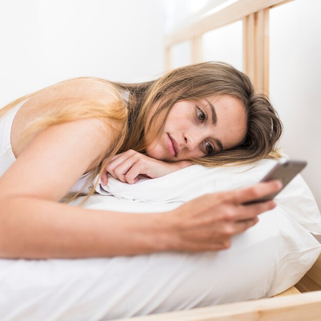 Женщина, лежа на кровати с помощью мобильного телефона