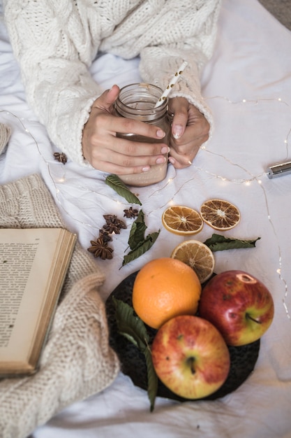 Woman lying on bed with cocktail and fruits