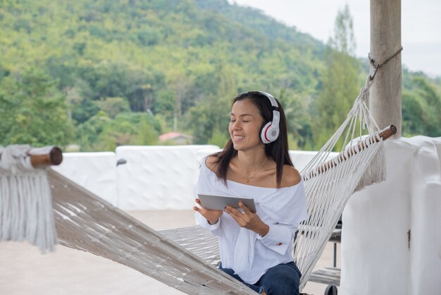 woman lying down on hammock listening to music with tablet