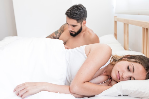 Женщина, лежащая перед своим мужем на кровати
