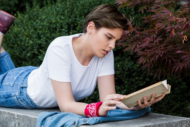 Woman lying on park parapet with book 