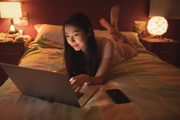横になってベッドでノートパソコンを使用している女性