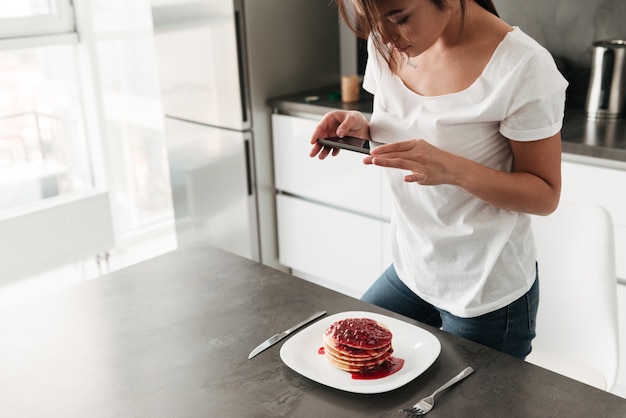 女性は、携帯電話でパンケーキの写真を作ります。