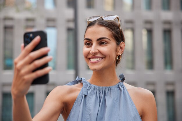  woman makes video call via smartphone while strolling in urban setting enjoys summer day has upbeat mood poses against blurred 
