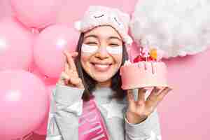 Foto gratuita la donna esprime un desiderio prima di soffiare le candeline sulla torta di compleanno incrocia le dita sorride felice vestita in pigiama festeggia il compleanno