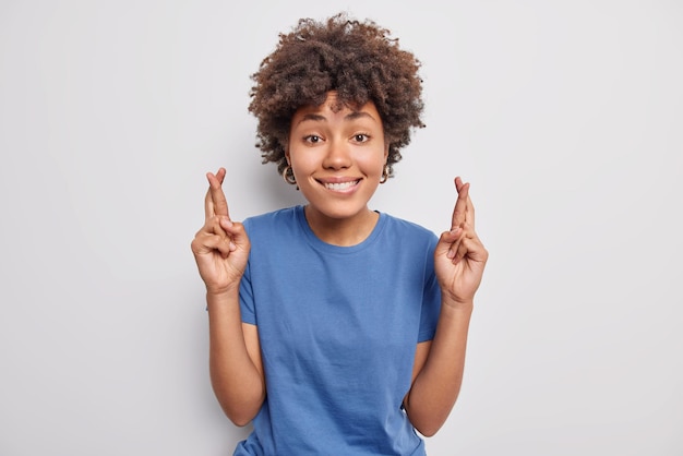 Foto gratuita la donna esprime un desiderio crede nella buona fortuna spera che i sogni si avverino morde le labbra ha un'espressione speranzosa indossa una maglietta blu casual isolata su bianco anticipa qualcosa