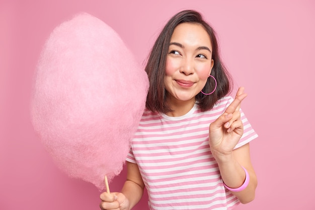 Free photo woman makes wish hopes dreams come true keeps fingers crossed wears casual striped t shirt holds tasty candy floss