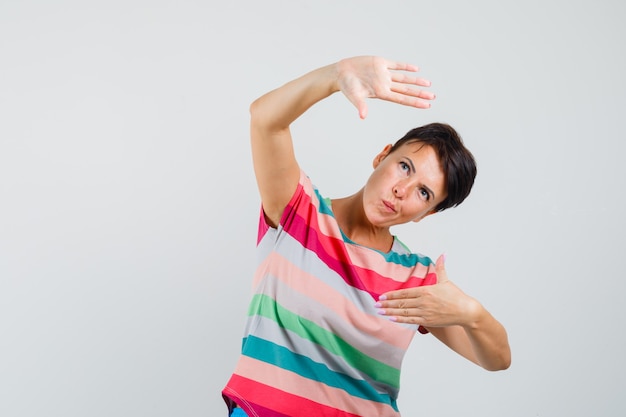 Женщина делает жест рамки в полосатой футболке и смотрит осторожно