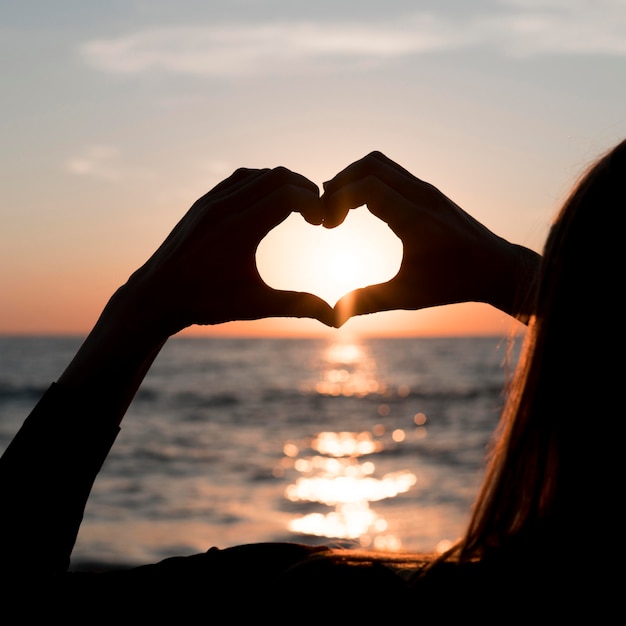 Woman making a heart at sunset