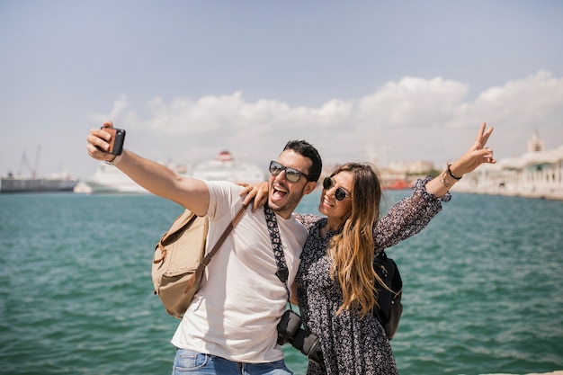 Free photo woman making peace sign with her boyfriend taking selfie on mobile