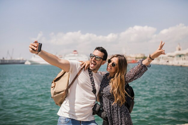Woman making peace sign with her boyfriend taking selfie on mobile
