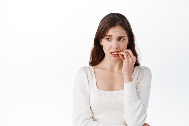 Woman making small mistake and being worried, standing alarmed against white wall