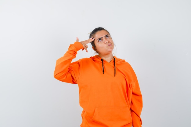 Woman making suicide gesture in orange hoodie and looking pensive