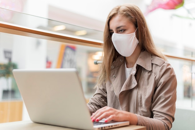 Free photo woman at mall working on laptop and wearing mask