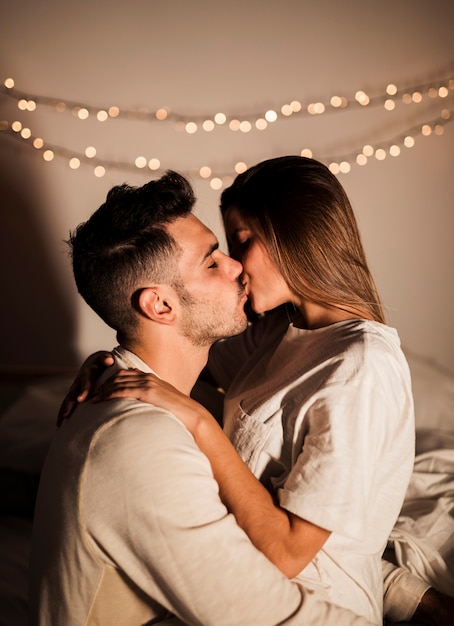 Woman and man kissing and embracing on bed in dark room