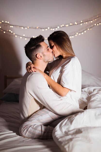 Woman and man kissing and hugging on bed in dark room