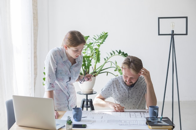 Woman and man looking at blueprint while working in office