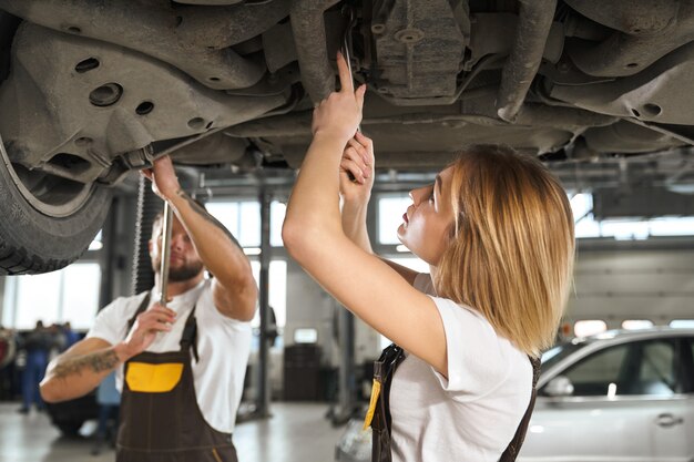 Woman and man mechanics repairing car undercarriage.