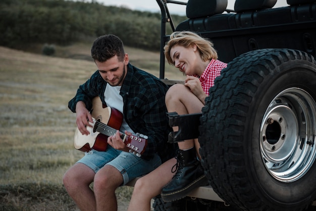 Woman and man playing guitar while traveling by car