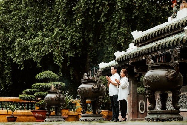 Free photo woman and man praying at the temple with burning incense