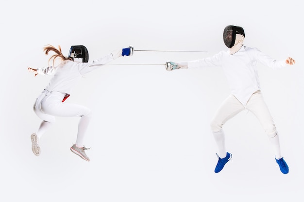 The woman and man wearing fencing suit practicing with sword against gray