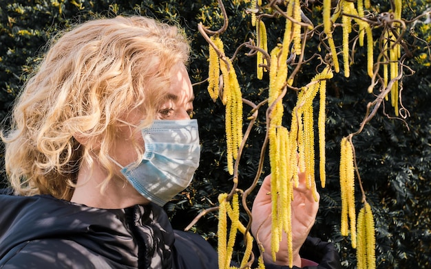 Free photo a woman in a mask touches a flowering hazel tree selective focus on the girl's eyes the concept of pollen allergy the main trigger of spring allergies