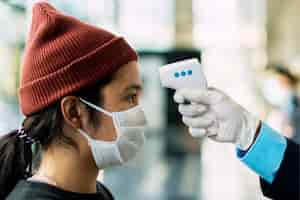 Free photo woman in a medical mask getting her temperature measured by an electronic thermometer