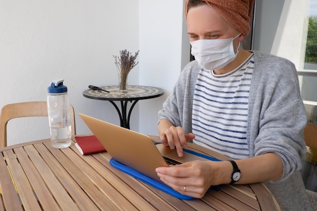 Donna nella mascherina della medicina che funziona con il computer portatile