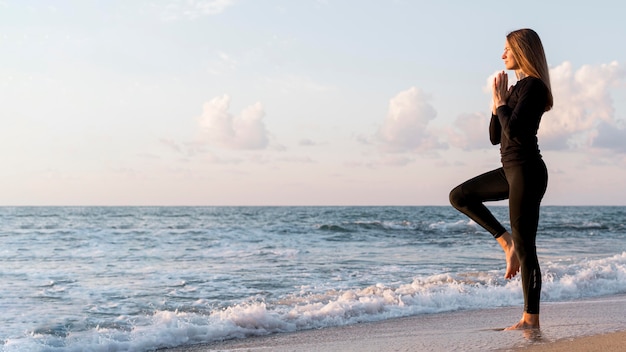 Free photo woman meditating on the beach with copy space