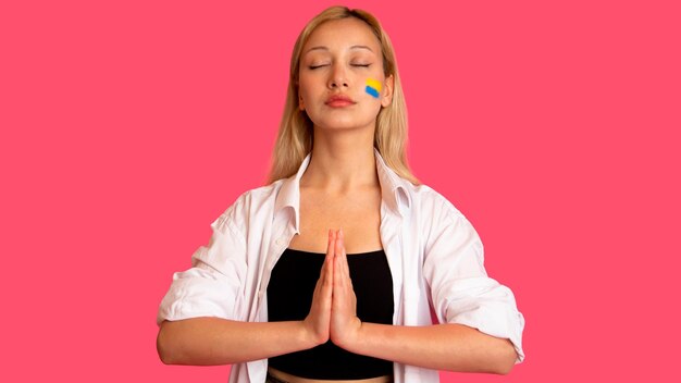 Free photo woman of model appearance with the flag of ukraine on her face holds posing on a pink background