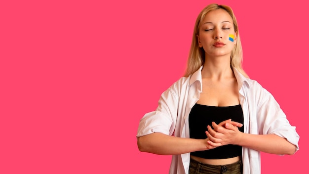 Woman of model appearance with the flag of Ukraine on her face holds posing on a pink background