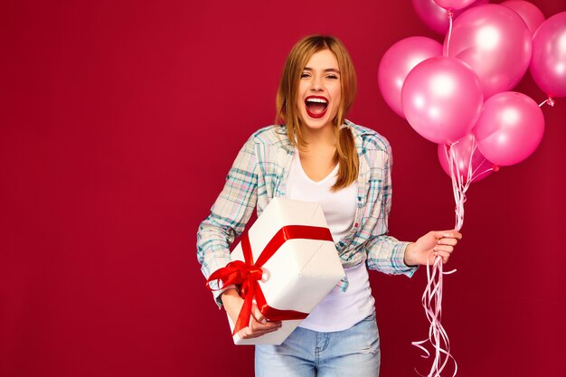 Женщина модель празднует и держит коробку с подарком и розовыми воздушными шариками