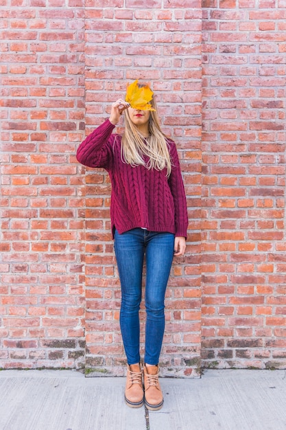 Free photo woman model reclining on brick wall and looking through fall leaf