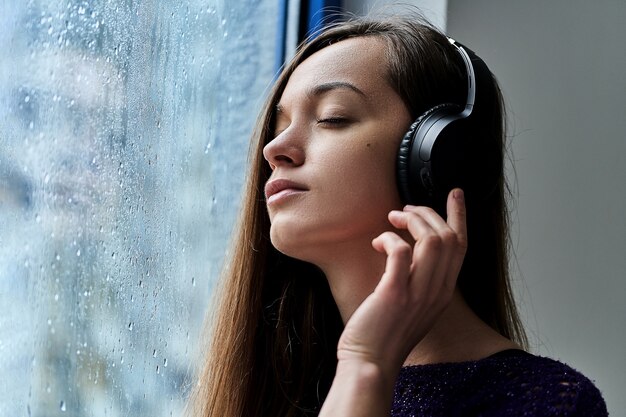 音楽を聴く 赤いニットのセーターを着ている ラップトップ フリーランサー 笑顔 幸せ ポジティブ タイピングで作業して ヘッドフォンでスマートフォンを使用して冬に自宅のソファーで魅力的な若者 無料の写真