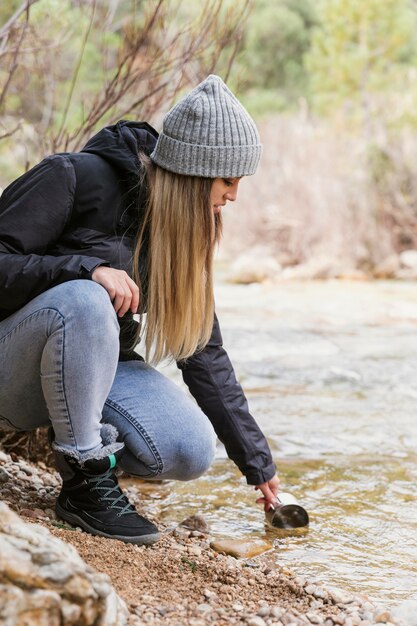 Женщина в природе пьет воду из реки
