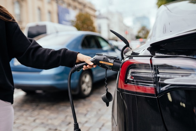 Woman near electric car. Vehicle charged at the charging station.