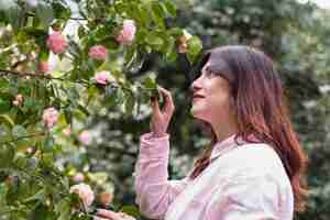 Foto gratuita donna vicino a molti fiori rosa che crescono su ramoscelli verdi