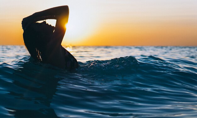 Woman in the ocean in the sunset time