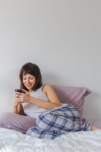 Бесплатное фото Женщина на кровати со смартфоном