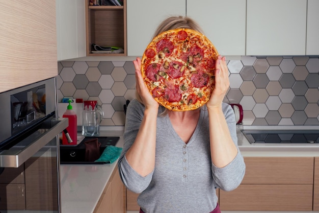Женщина открывает печь и нарезает пиццу с помидорами, оливками, грибами и сырной колбасой