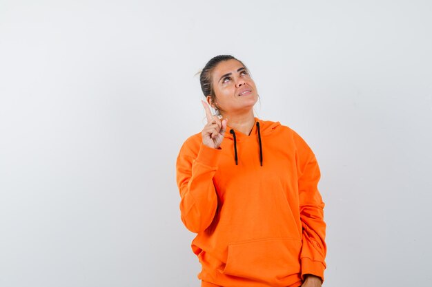 Woman in orange hoodie pointing up and looking grateful