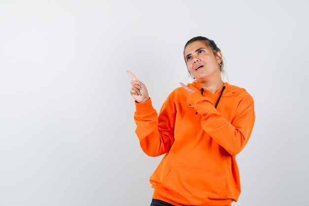 woman in orange hoodie pointing at upper left corner and looking dreamy