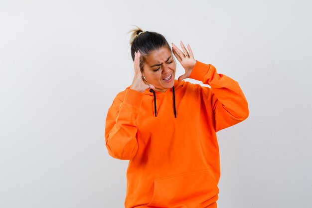 Woman in orange hoodie raising hands in aggressive manner