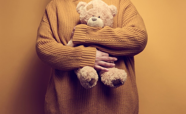 Woman in orange knitted sweater hugs cute brown teddy bear. the concept of loneliness and sadness, depression
