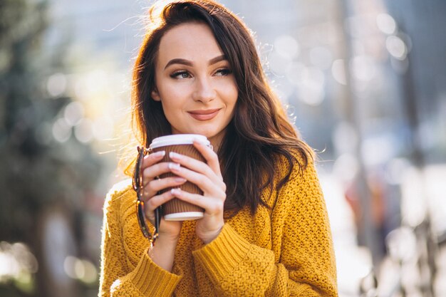 Женщина в оранжевом свитере пьет кофе