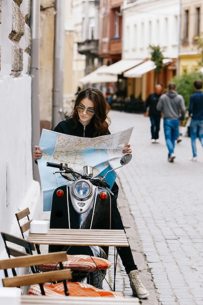 Foto gratuita la donna in occhiali da sole originali si siede sullo scooter con la mappa turistica