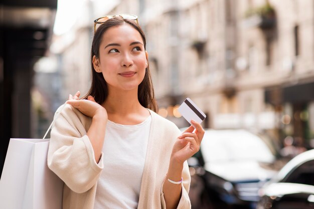 Woman outdoors holding credit card and shopping bag