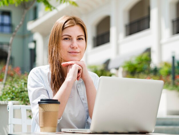 Woman outdoors with coffee working on laptop